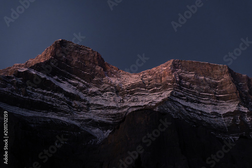 Billede på lærred Alpenglow Warm Light on Snow-Streaked Rocky Mountain Peaks Against Deep Blue Nig