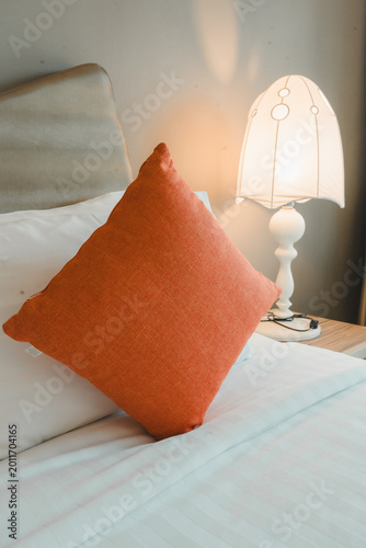 Cozy bedroom with an orange cushion and a small bedside table with a lamp