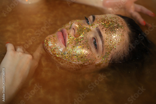 Φωτογραφία Portrait of a beautiful dark-haired young girl in golden water with a gold glitt
