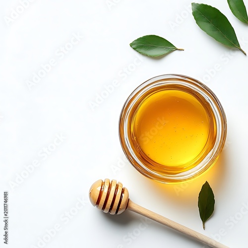Glass jar of golden honey with wooden dipper and green leaves on white background