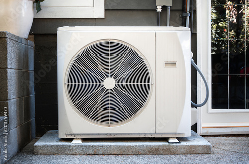 Heat pump outside of home. All-electric HVAC system for heating and cooling with thermal energy transfer. Modern high efficiency heating system on concrete slab. Vancouver, BC. Selective focus.
