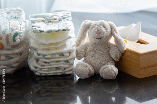 Stack of diapers with a toy bunny and a box of napkins on the table. Newborn nappies concept, highlighting baby products, diaper promotions, or child care