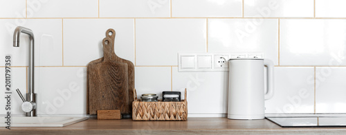 Minimal kitchen interior with stainless steel faucet, wooden cutting board and electric kettle on countertop. Contemporary Scandinavian kitchen with copy space.