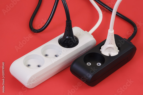 Red background with black and white power strips adapters with plugged cables. The concept of electricity, energy connection, power delivery and sharing