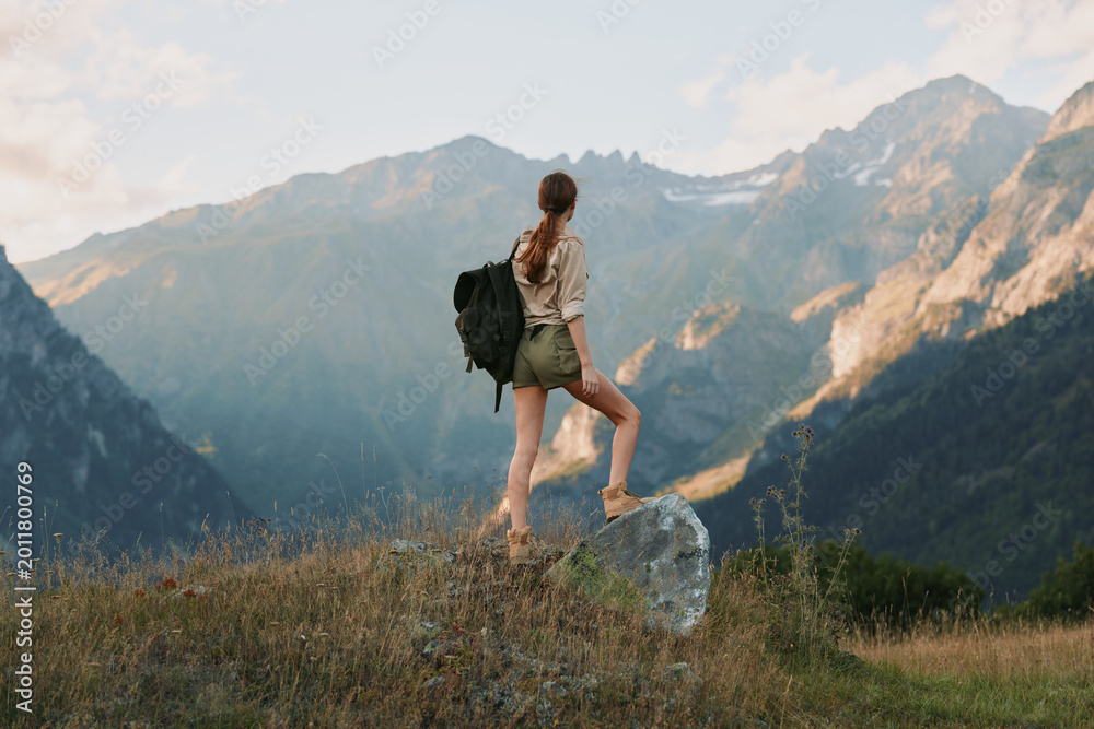 Naklejka premium Woman hiking outdoors with backpack in a mountain landscape, capturing a sense of adventure, balance, and nature in a sunlit breeze and expansive scenery