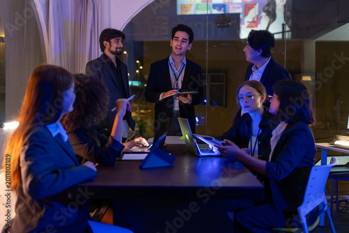 Diverse business team having meeting and brainstorming in modern dark office. Executive male leader presenting data to office employees during night shift collaboration in workplace