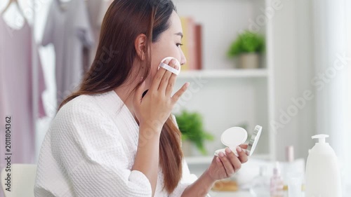young Asian women applying foundation makeup using cosmetic sponge puff for facial beauty skincare morning routine in bathroom home preparing for work day