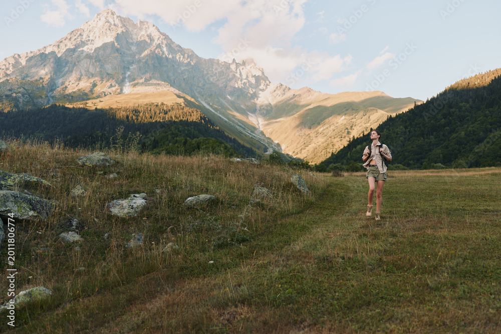 Naklejka premium Woman hiker stands in a grassy valley with rugged mountains in the background, wearing hiking gear. A lifestyle moment of outdoor exploration and adventure.