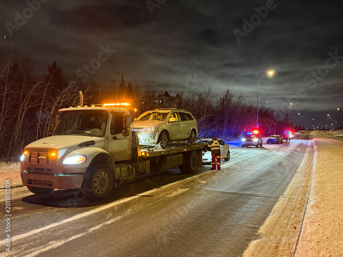 Photos Tow truck loading a disabled vehicle on a snowy roadway at night with police vehicles responding in Alberta, Canada