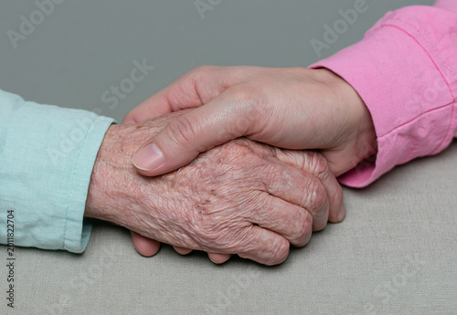 Elderly and young hands clasped together in warm intergenerational gesture of comfort and support, palliative care concept, gray background