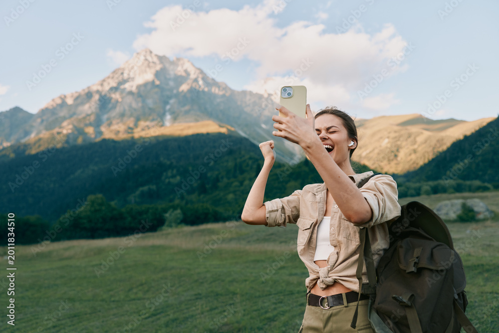 Fototapeta premium Selfie taking hiker woman with backpack smiles in the mountains during daytime outdoors