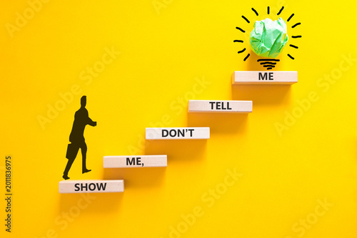 Tell or show symbol. Concept words Show me, do not tell me on beautiful wooden blocks. Beautiful yellow paper background. Light bulb icon. Businessman icon. Business tell or show concept. Copy space.