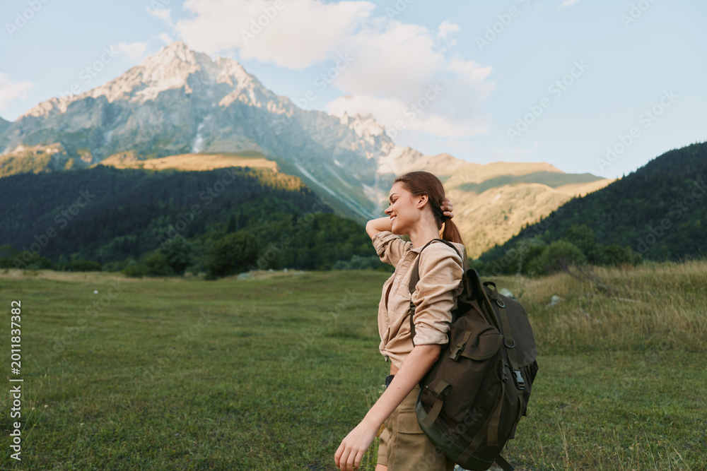 Fototapeta premium Bright woman outdoors hiking backpack nature mountain scenery travel leisure, enjoying sunny day with relaxed posture and meadow backdrop