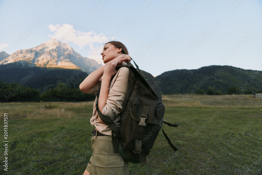Fototapeta premium A young woman with a backpack walks across a meadow toward distant mountains, feeling free, focused, curious, and ready for adventure.