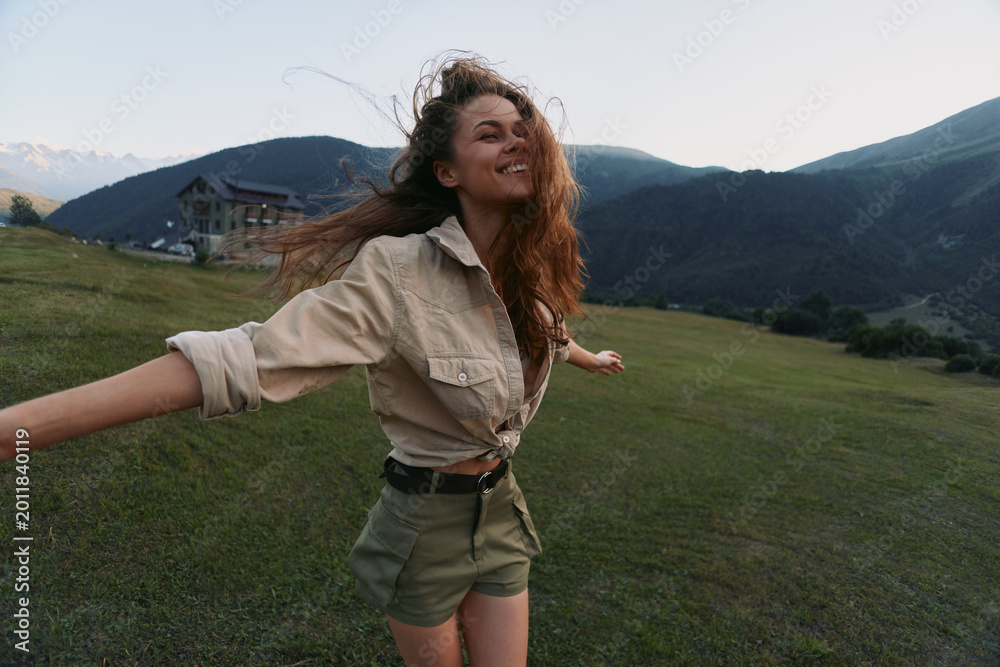 Naklejka premium Smiling woman with long hair wearing a beige shirt and khaki shorts in a grassy field, capturing an outdoor lifestyle moment filled with happiness and nature. Bright mood and color