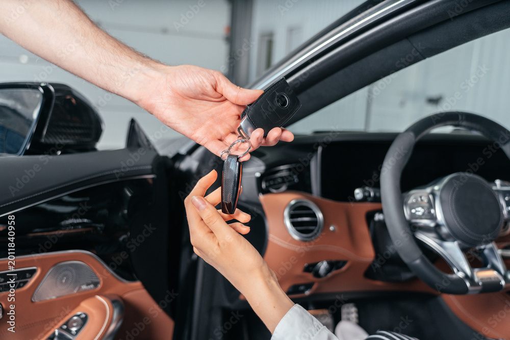 Naklejka premium Car dealer is giving key for a new car to young woman