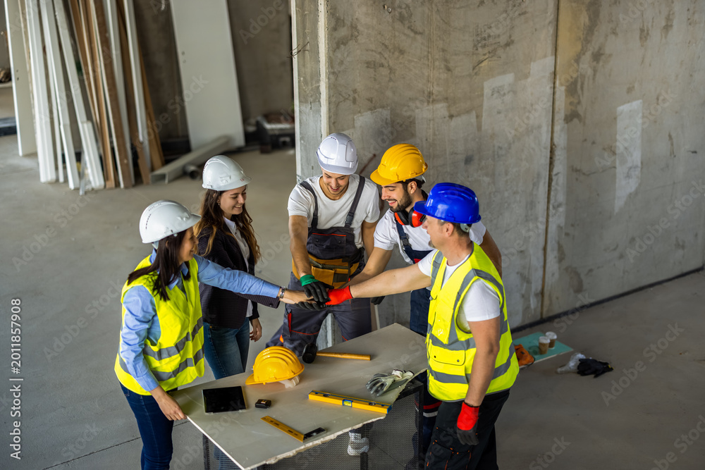 Fototapeta premium Unified construction team putting hands together in a huddle over a table on site.