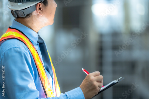 Canvastavla A focused quality control inspector in safety gear and hard hat meticulously recording data on a clipboard in an industrial plant environment