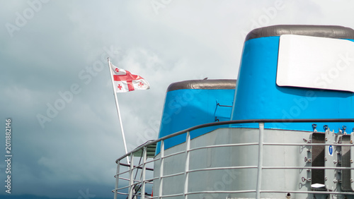 Фотография ship upper deck featuring blue funnels and the Georgian national flag waving aga