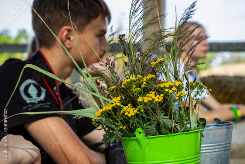 Obraz na płótnie teenage boy sits behind a bouquet of tansy and herbaceous field plants in an ope