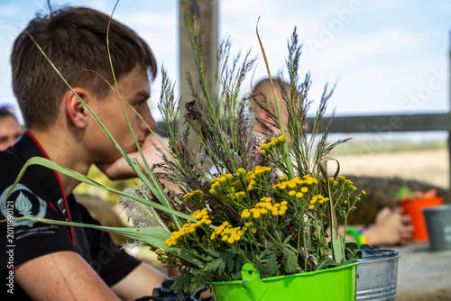 Obraz na płótnie teenage boy sits behind a bouquet of tansy and herbaceous field plants in an ope