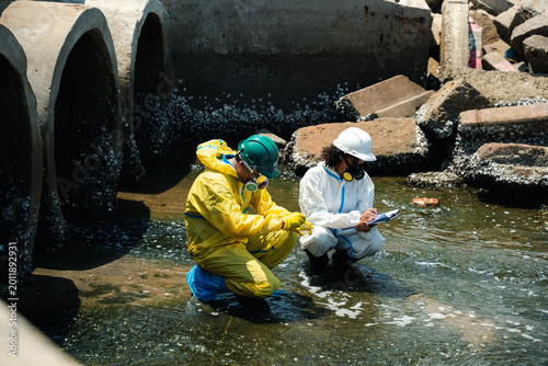 Hazmat workers in protective suits inspecting polluted wastewater drainage tunnel and contaminated industrial water during environmental hazard response operation