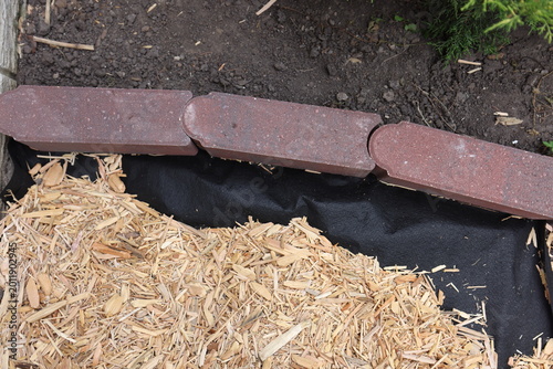 Putting in a bed in the garden with a red brick edge and mulch that has black barrier fabric below. 