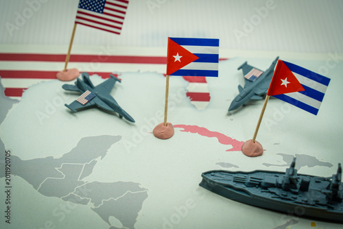 United States and Cuba flags on a world map with miniature jets and a battleship, symbolizing USA president Maximum Pressure Campaign on Cuba