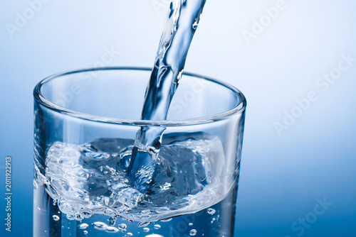 Pouring water into glass on blue background