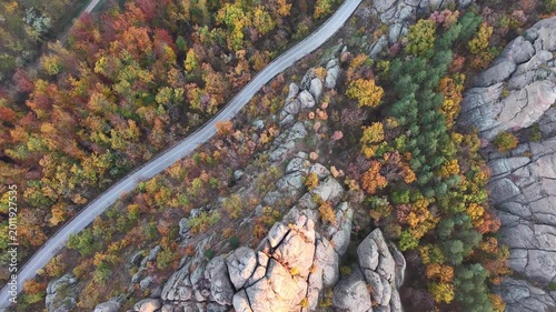Overhead aerial view of a curving road through colorful autumn woodland and rocky terrain.
