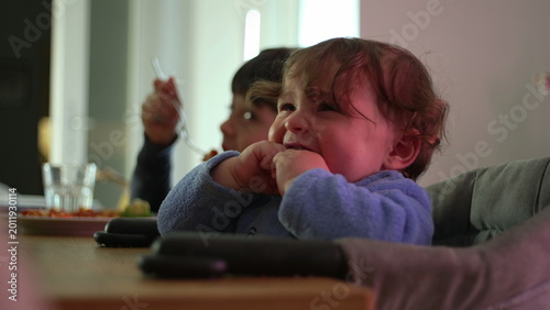 Fotografie Frustrated toddler in blue outfit sitting in high chair showing discomfort and e