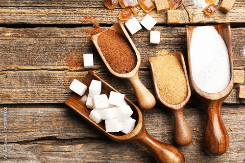 фотографія Different types of sugar in scoops on wooden table, flat lay