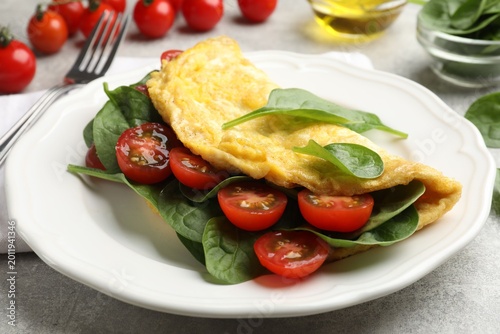 Schilderij op canvas Tasty omelette with spinach and tomatoes served on light grey table, closeup