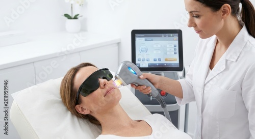 Aesthetician performing laser skin treatment on a woman's face with protective eyewear in a modern clinic.