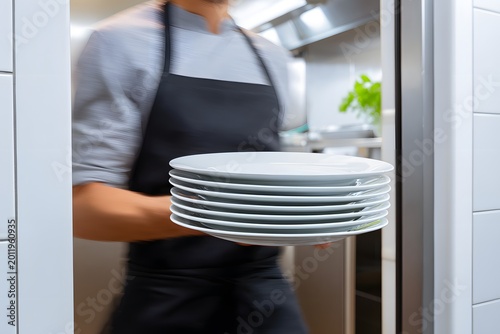 Waiter moves through the kitchen holding several clean white plates in hand