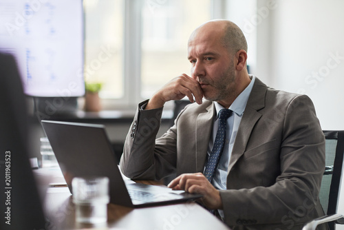 Foto Adult businessman working on laptop, thinking through problem during office analysis and decision making