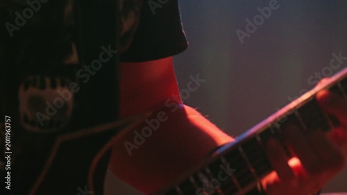 The musician's hand plays on neck of the guitar. The blue lighting of stage creates a gloomy atmosphere of a rock concert. Soft focus and dynamic perspective of live performance and musical energy