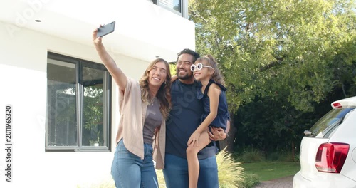 Family posing at driveway while mother raising phone for selfie daughter adjusting sunglasses