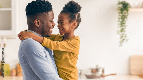 Tableau sur toile A man and a young girl smile at each other while the girl hugs him in a kitchen