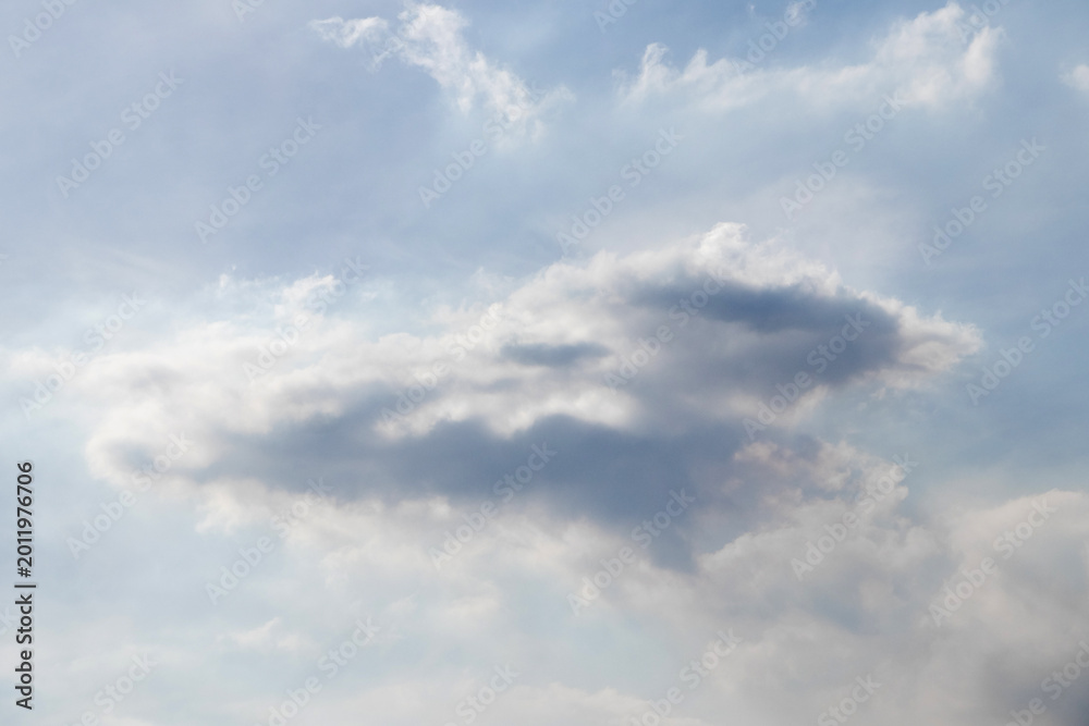 Obraz premium Cloudy sky with a large dark gray cloud in the center and light white clouds around, soft daylight, calm atmosphere