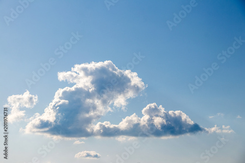 Blue sky with a large fluffy white cumulus cloud in the center of the frame, bright daylight, light and calm atmosphere
