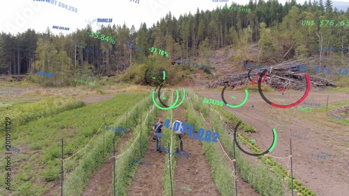 Two co-workers stepping into trellised rows, inspecting crops for harvest, AR gauges tracking zones