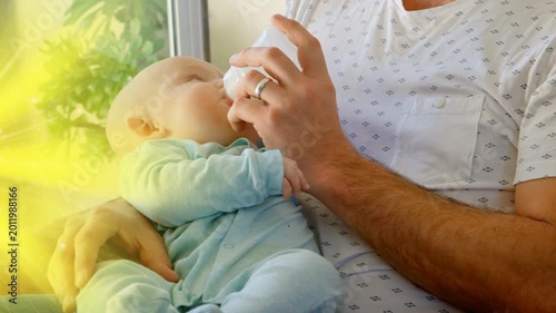 Mature caregiver offering bottle and adjusting infant beside window, promoting childcare bonding