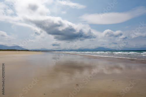 Foto Vast Sandy Beach with Reflective Shoreline, Rolling Waves, and Distant Mountains