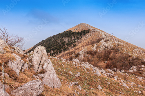 Slika na platnu Rugged mountain landscape with a prominent peak, dry grass, exposed rocks, and a
