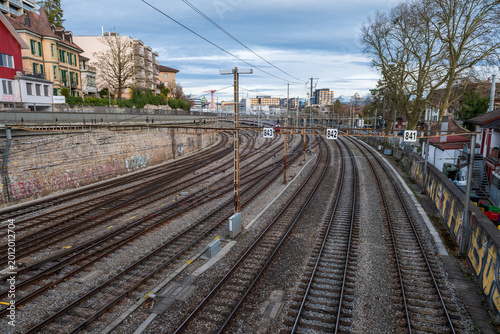 Curving train tracks with catenary wires and urban buildings under cloudy sky in Bern, Switzerland.