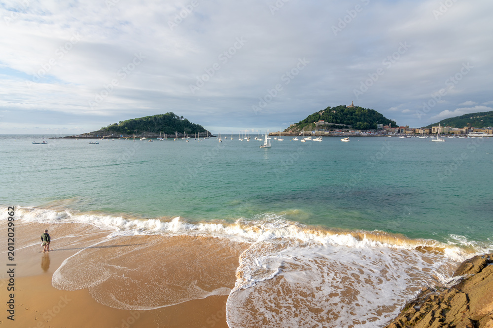 Fototapeta premium Sea foam reaching the sandy shore at Ondarreta beach with panoramic coastal scenery in San Sebastian, Spain.