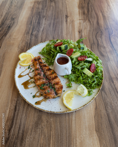 Grilled salmon fillet with fresh green salad and lemon on wooden table
