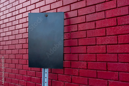 Blank black sign on red brick wall. Mockup of empty signage against painted brickwork