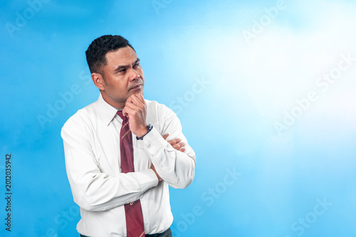 Φωτογραφία Portrait of a pensive Indonesian office worker in white shirt and tie, holding his chin while thinking deeply